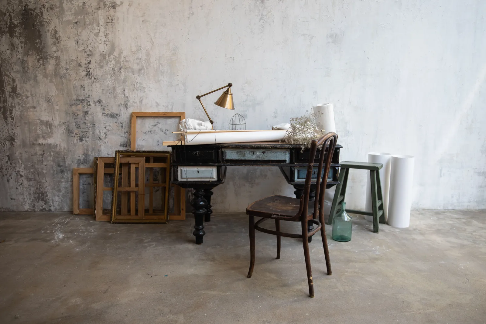 A rustic art studio featuring a vintage desk, wooden chair, and abstract frames on a textured wall