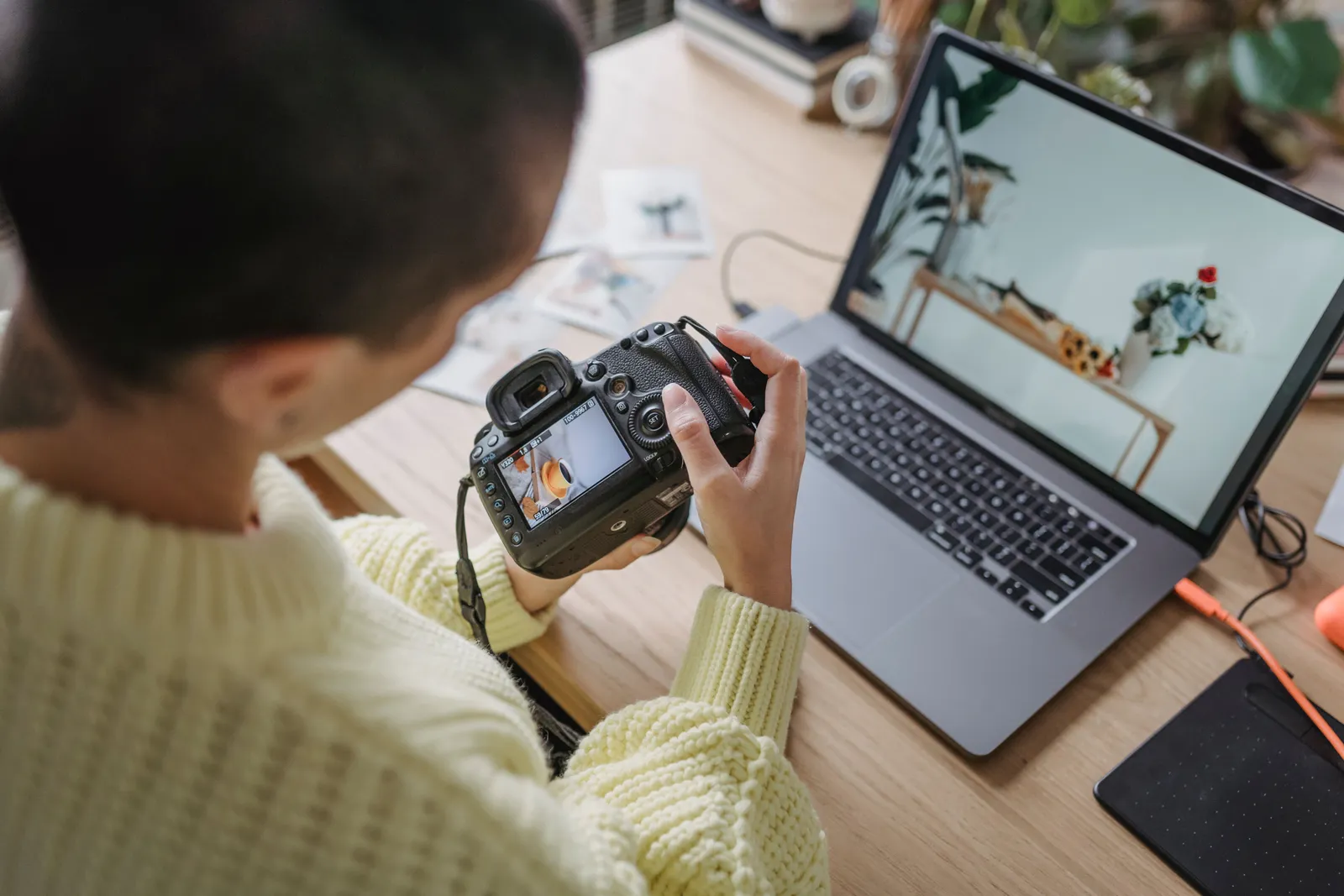 From above of crop anonymous female photographer looking at screen of photo camera with photo while sitting at table with