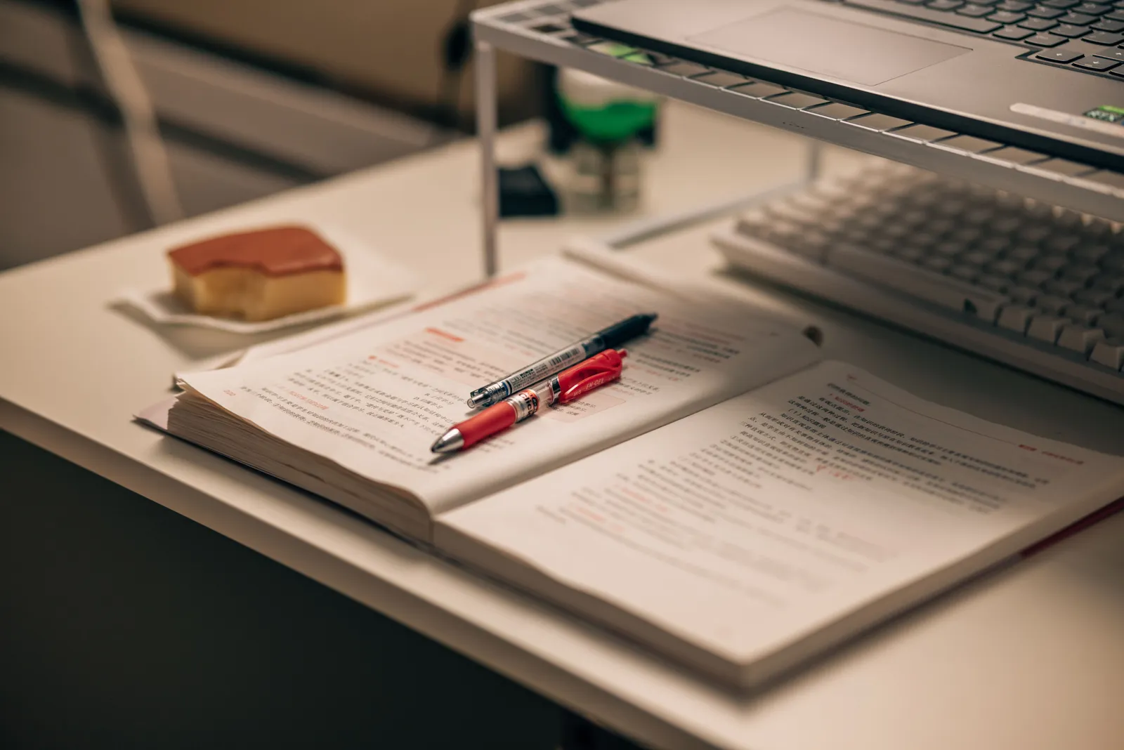 Open book with study notes, pens, and a laptop on a desk creating a focused study environment
