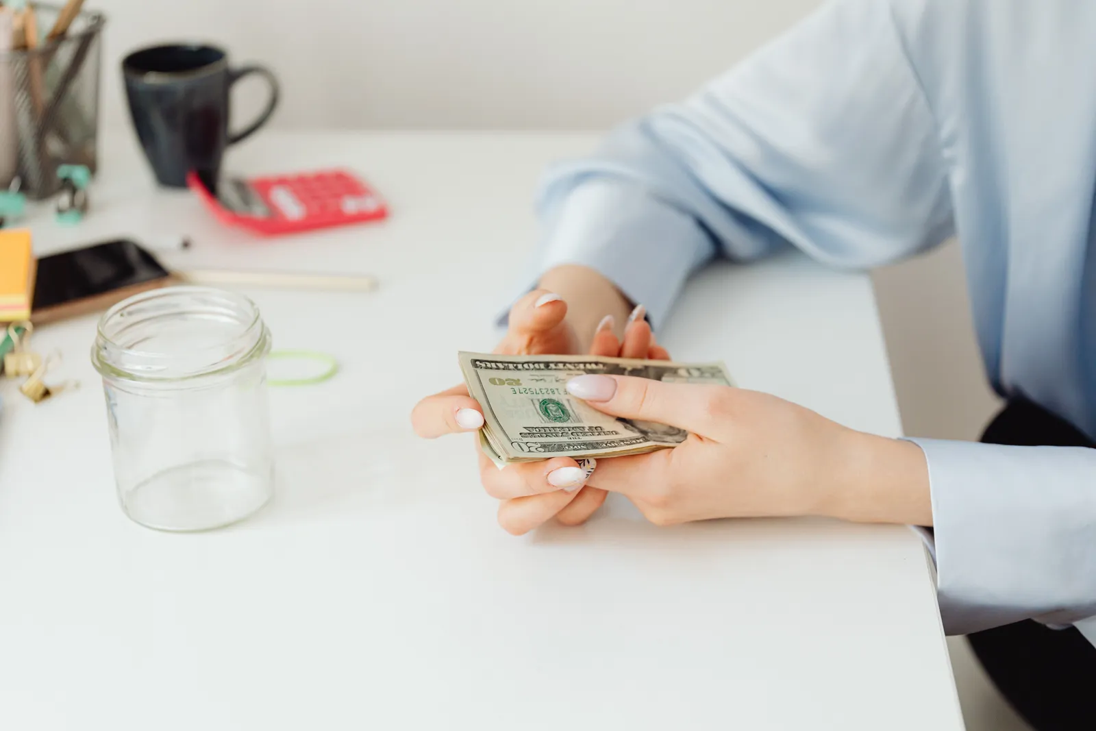Close-up of hands counting US dollar bills on a white desk with office supplies