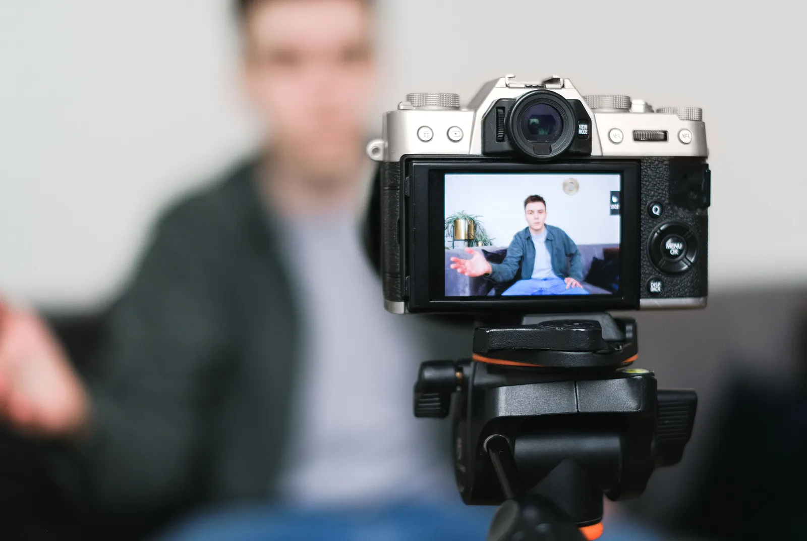Man recording a vlog indoors using a mirrorless camera on a tripod with selective focus