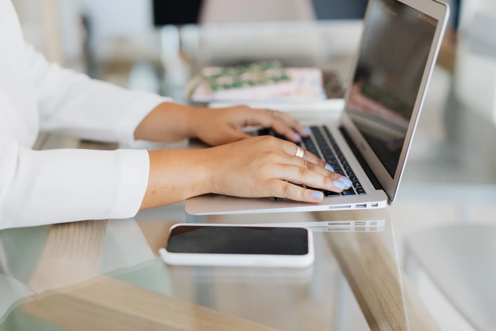 Close-up of hands typing on a laptop with smartphone on desk