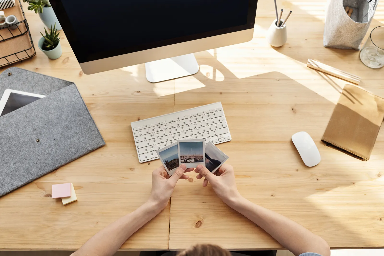 A cozy home office desk setup with hands holding printed photos, capturing a moment of nostalgia and creative inspiration