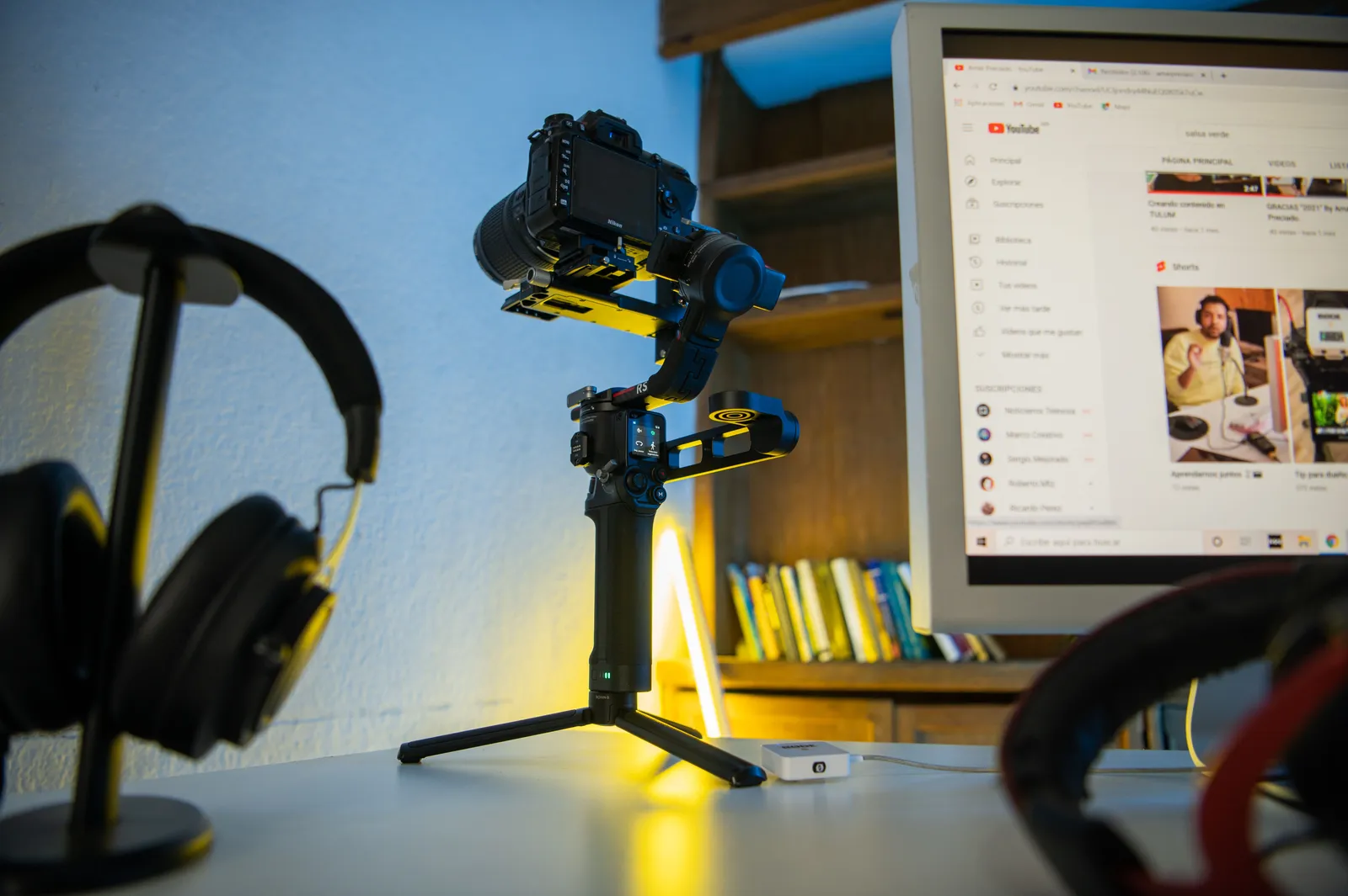 Professional photography setup featuring a camera on a tripod, headphones, and a computer monitor displaying video content