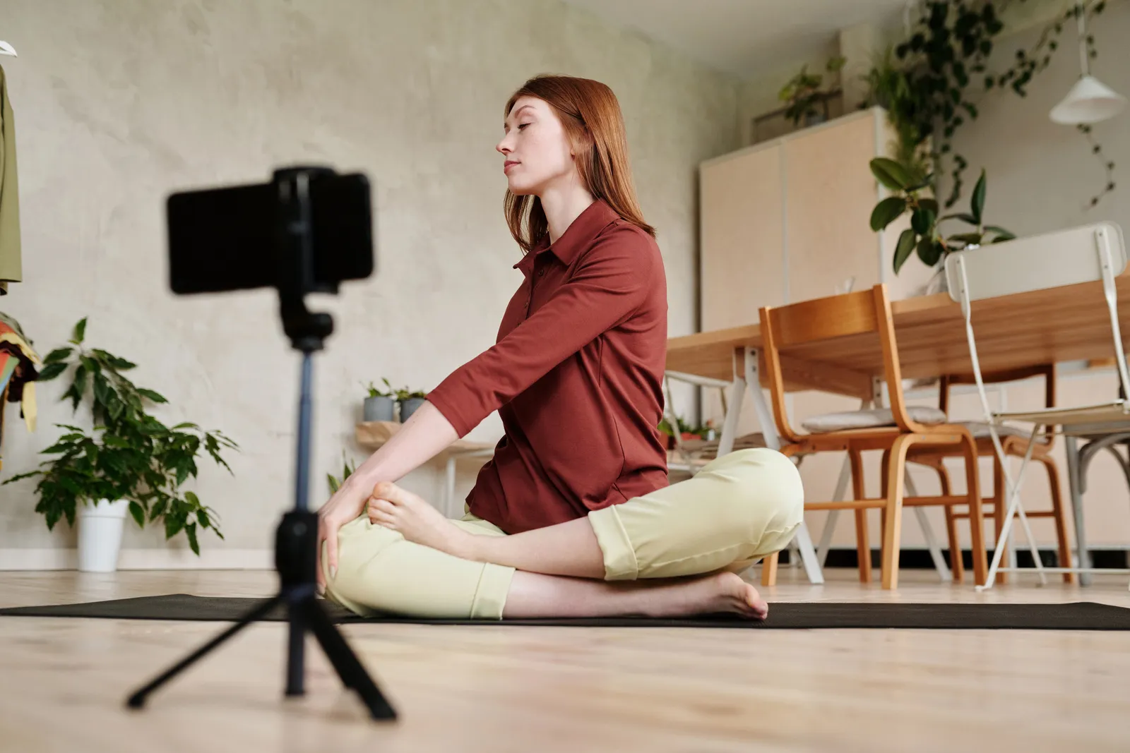 Young woman doing yoga at home, recording with smartphone on tripod