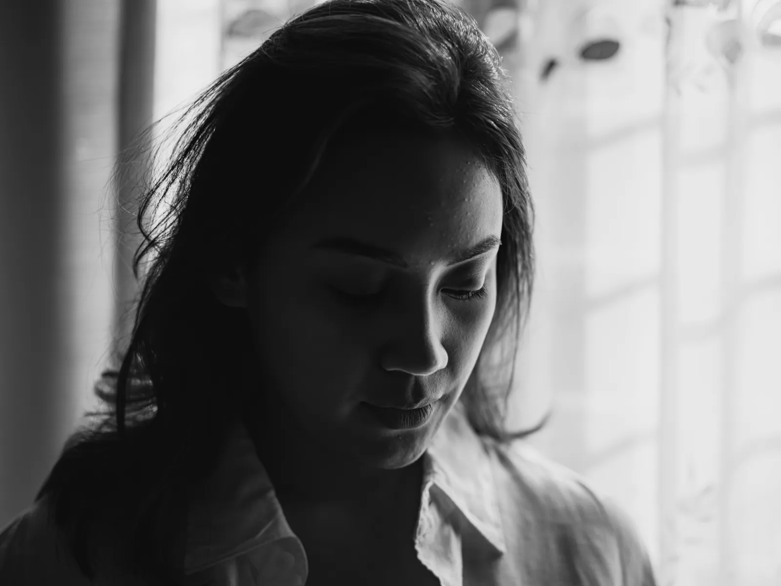 Monochrome portrait of a woman with soft lighting, capturing a pensive expression near a window